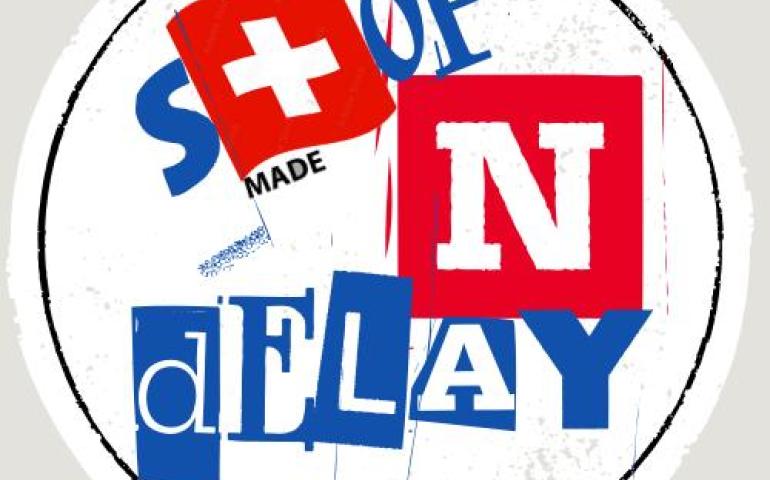 Stop N Delay yazısının T harfi İsviçre bayrağı ile ifade edilirken üstünde swiss altında da made yazılı ki N harfiyle birlikte made in swiss olmuş oluyor. en altında mülteci hakları insan hakklarıdır yazılı.