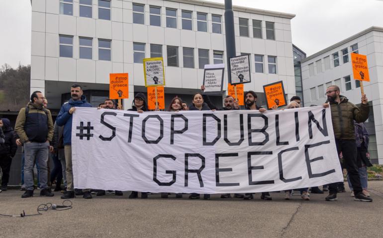 Sem binası önündeki basın açıklamasından bir fotoğraf. Pankartta Stop Dublin Greece yazılı ve arkada eylemciler var